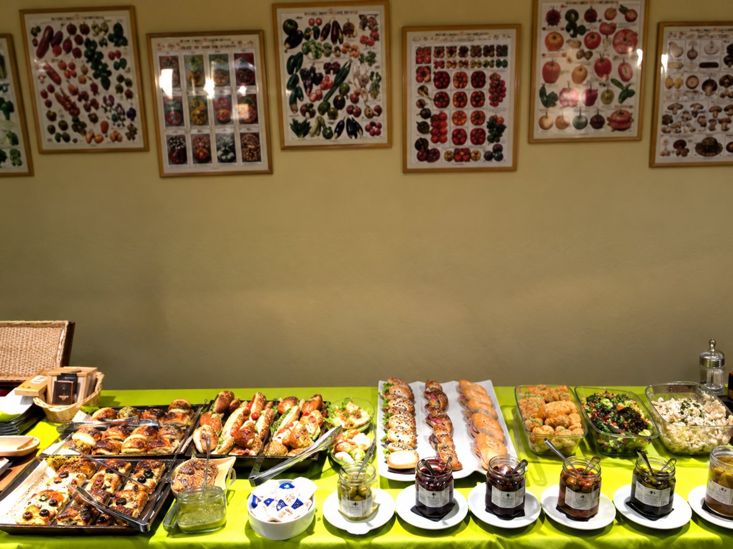 Un comptoir de buffet présente des sandwichs, des viennoiseries et des bocaux devant un mur décoré de plusieurs affiches encadrées.